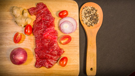 Fresh meats, vegetables and spices are laid out on a food prep table covered with a black tablecloth.の写真素材