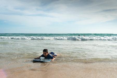 The waves swept the surf boy toward the shore.boy surfing on white waves.Paradise beach blue sea, and clear sand landscape background.smiling face of happy boy surfing concept.の写真素材