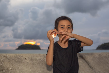 A boy holding a crystal ball beside wave barrier at Kata beach Phuket Thailand.
cloud above island in sunset background.
smiling face of happy boy relax concept.の写真素材