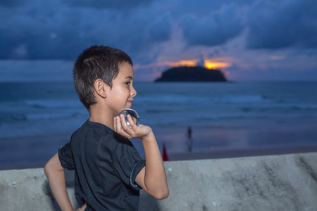 A boy holding a crystal ball beside wave barrier at Kata beach Phuket Thailand.
cloud above island in sunset background.
smiling face of happy boy relax concept.の写真素材