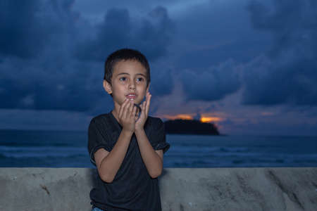 A boy holding a crystal ball beside wave barrier at Kata beach Phuket Thailand.
cloud above island in sunset background.
smiling face of happy boy relax concept.の写真素材