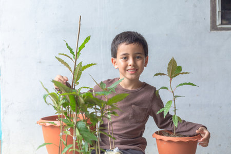 A happy boy enjoy with his Kratom tree seedlings. 
A cute boy sat hugging a tree with happy smile. feeling happy smiley face, love the trees. 
smiling face of happy boy relax save the earth concept.の写真素材