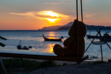 lonely Teddy Bear sitting on a swing in front Rawai beach to see sunrise.
scenic reflection of beautiful sunshine above fishing boats are floating in the Rawai sea.
beautiful golden sky background.の写真素材