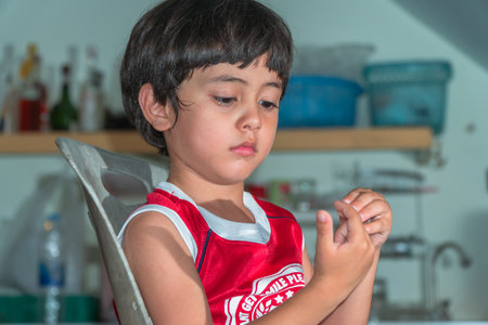 A boy wear red shirt sitting in the kitchen during waiting for a mealの写真素材