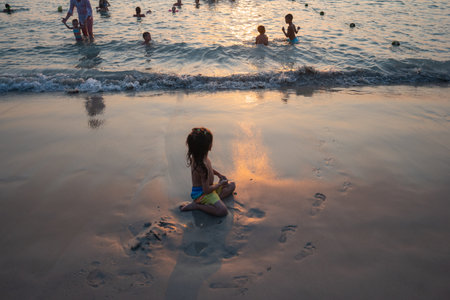 A cute boy with long hair playing in the sand on the beach in sunset. 
His carefree attitude is contagious, and everyone was drawn in by his joy. 
He was a symbol of hope and innocence.の写真素材
