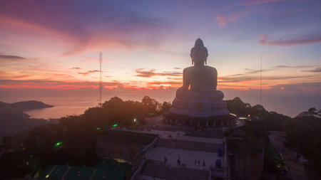A striking silhouette of the Big Buddha statue set against a vibrant dusk sky into the horizon. The statue overlooks a peaceful coastal landscape, creating a tranquil and reflective atmosphere.の写真素材