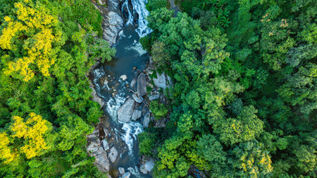 A stunning aerial view of a cascading waterfall surrounded by vibrant green forest and rolling hills. The scene captures the beauty of nature's raw powerの写真素材