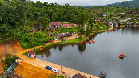 Aerial view of tranquil lakeside village nestled in lush, mist-covered hills under an overcast sky....
