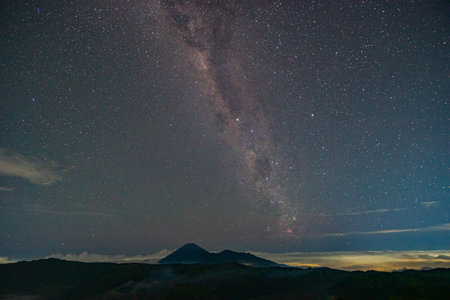 Time lapse The Milky Way spins over Mount Bromo volcanoes. The Milky Way sparkles above the summit of Bromo Volcano and stands perpendicular to the summit of Mount Bromo spewing white smokeの写真素材