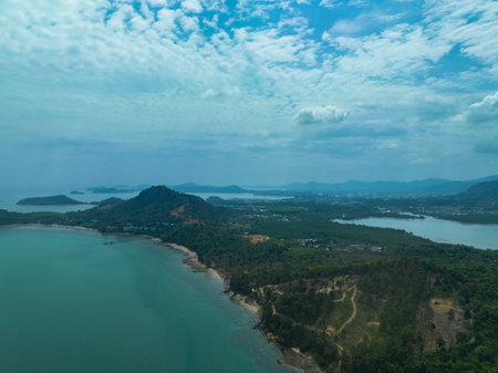 A breathtaking aerial view of a lush green coastline with winding paths, crystal-clear turquoise waters, and distant islands under a partly cloudy sky. green seaの写真素材