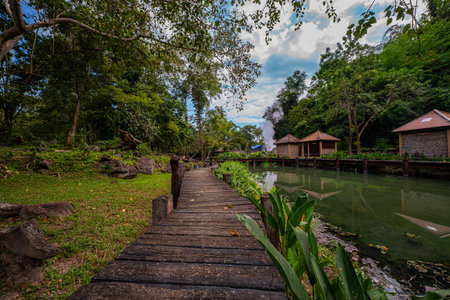 Fang hot spring. A scenic view of a natural hot spring emitting steam in a lush tropical forest. The vibrant greenery, blue sky, and traditional wooden create a tranquil and refreshing atmosphereの写真素材