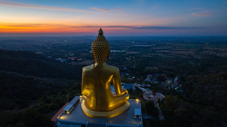 An awe-inspiring view of a big golden Buddha statue atop a hill overlooking a serene valley, captured during the vibrant colors of sunset. aerial view of The biggest golden Buddha at Lopburi Thailandの写真素材