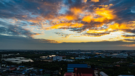 An aerial perspective showcasing a stunning Thai temple complex with intricate golden spires, surrounded by urban and rural landscapes under a cloudy blue sky.の写真素材