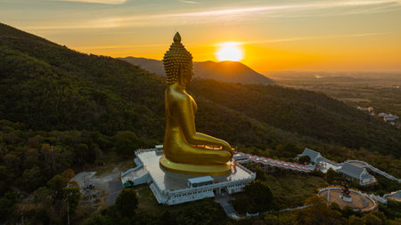 An awe-inspiring view of a big golden Buddha statue atop a hill overlooking a serene valley, captured during the vibrant colors of sunset. aerial view of The biggest golden Buddha at Lopburi Thailandの写真素材