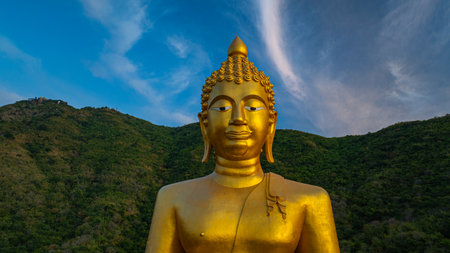 An awe-inspiring view of a big golden Buddha statue atop a hill overlooking a serene valley, captured during the vibrant colors of sunset. aerial view of The biggest golden Buddha at Lopburi Thailandの写真素材