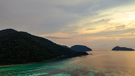 Aerial view of a stunning sunset above the Surin Islands. With golden hues reflecting on the calm ocean waters. The coral reef at the shoreline in the foreground adds depth. Paradise for snorkelの写真素材