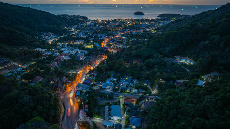 An aerial view of a town at dusk, with vibrant lights illuminating the streets and buildings. Lush greenery and hills frame the scene, creating a serene and tranquil landscape.の写真素材