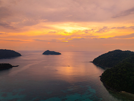 A breathtaking aerial view of tropical islands surrounded by calm ocean waters at sunset. The golden hues of the sky reflect on the water, creating a tranquil and picturesque seascape.の写真素材