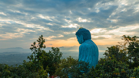 A serene aerial view of a large Buddha statue surrounded by lush forest, with a stunning sunrise casting vibrant hues over a misty mountainous landscape in the background. beautiful sky at sunrise.の写真素材