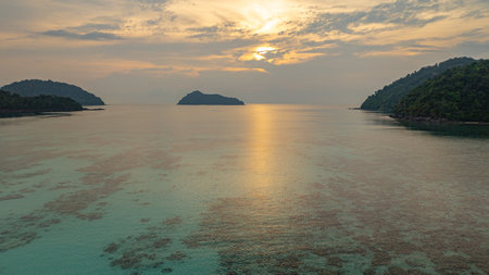 Aerial view of a stunning sunset above the Surin Islands. With golden hues reflecting on the calm ocean waters. The coral reef at the shoreline in the foreground adds depth. Paradise for snorkelの写真素材