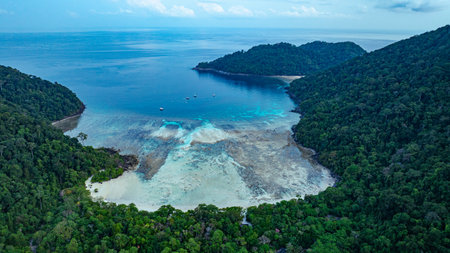 A stunning bird's eye view of Ao Mai Ngam, Surin Islands, a horseshoe-shaped white sand beach surrounded by lush green forest, coral reefs and schools of fish, a popular destination for divers.の写真素材