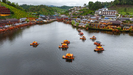 Aerial view of a tranquil mountain village nestled by a reflective lake at dusk, with warm lights...