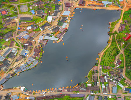 aerial top view of a lakeside village, showcasing a mix of rustic architecture, lush greenery, and boats scattered across the calm water. A harmonious blend of natural beauty and human settlement.の写真素材