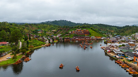 Aerial view of tranquil lakeside village nestled in lush, mist-covered hills under an overcast sky. The calm water reflects the vibrant buildings, raft creating a serene and picturesque scene.の写真素材