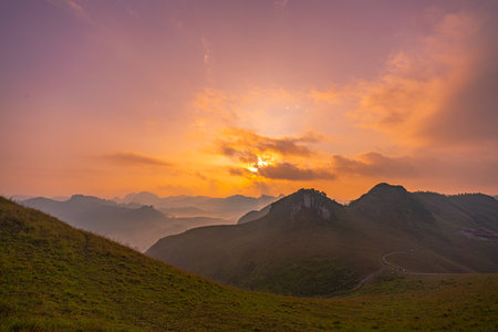 Aerial view of serene sunset casts a golden glow over rolling hills and distant mountain peaks, creating a peaceful and atmospheric landscape with layers of mist and soft light. mountain background.の写真素材