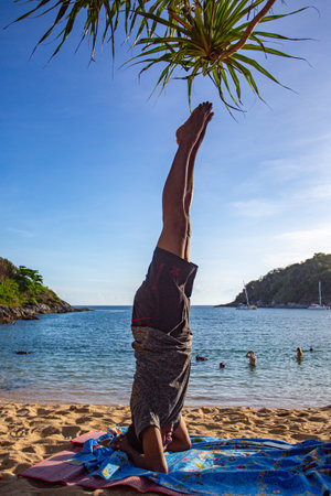 A man doing yoga in a headstand pose by the sea. Yanui Beach is a small, quiet beach with a small island in front of the clear blue water. It is a great place for snorkeling and relaxing.の写真素材