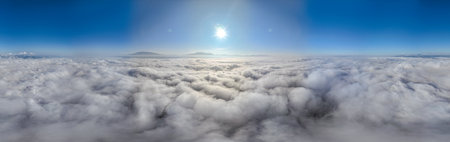 A serene view of the early morning sun rising above a vast sea of clouds, with distant mountain peaks faintly visible on the horizon, creating a peaceful and ethereal landscape. Flying over the cloudの写真素材