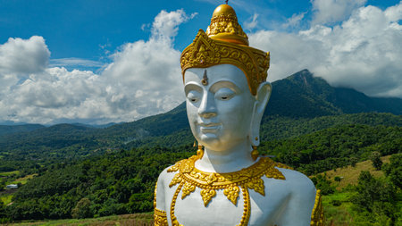 Close up the Tall Buddha Brahma Panyo statue standing tall in front of Doi Luang mountain, adorned in golden details stands serenely amidst lush green mountains and cloudy skies, Chiang Mai provinceの写真素材