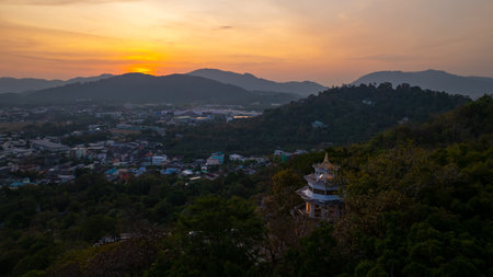 Aerial view of Sunset above Khao Rang viewpoint. view of a town nestled among lush green mountains at sunset, with a Pavilion structure perched on the hillside at Phuket town at Duskの写真素材