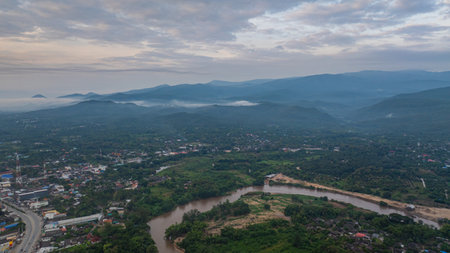 A stunning aerial view of a winding river flowing through a vast rural landscape at dawn. The soft morning light and misty atmosphere create a tranquil and picturesque scene, with scattered villagesの写真素材