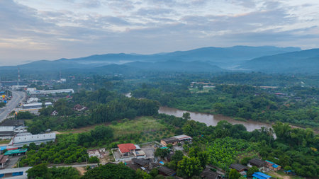 A stunning aerial view of a winding river flowing through a vast rural landscape at dawn. The soft morning light and misty atmosphere create a tranquil and picturesque scene, with scattered villagesの写真素材