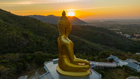 An awe-inspiring view of a big golden Buddha statue atop a hill overlooking a serene valley, captured during the vibrant colors of sunset. aerial view of The biggest golden Buddha at Lopburi Thailandの写真素材