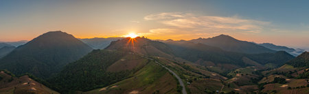 Aerial view of Rays of light burst from the mountain peaks in the morning.The beautiful sunrise casts a golden glow over the green hills. casting a warm glow across the lush landscape. amazing viewの写真素材