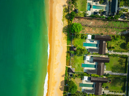 A stunning aerial view of a tropical coastline featuring golden sandy beaches, lush green pine trees, and turquoise ocean waves crashing against the shore. perfect for travel and nature visuals.の写真素材