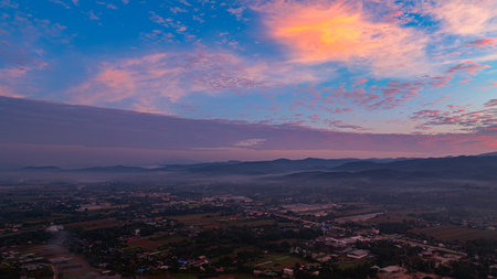 A breathtaking sunrise illuminates a small village nestled among lush green fields and karst mountains, with vibrant clouds filling the sky. The harmony of rural life set dramatic natural formationsの写真素材