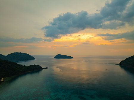 Aerial view of The sun sets at Ao Mai Ngam, Surin Islands. The reflection of the setting sun.while the silhouette of lush green hills and anchored sailboats enhance the peaceful ambianceの写真素材