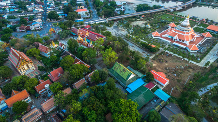 An aerial view showcasing a large, beautifully designed riverside temple complex with traditional Thai architecture, surrounded a winding river, and a modern bridge connecting nearby communities.の写真素材