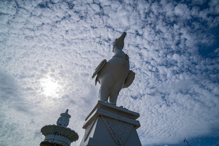 The sculpture at the Karon Beach roundabout in Phuket stands beneath a sky filled with small, fluffy clouds, gently diffusing the sunlight and casting a soft light over the scene. Fluffy cloudの写真素材