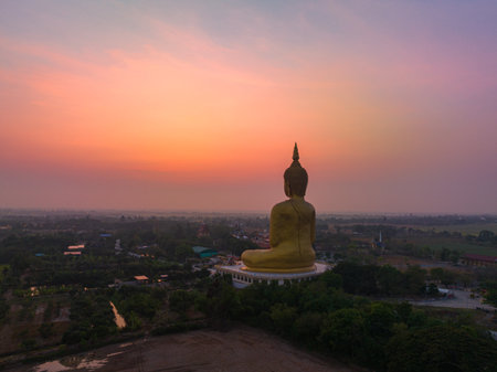 aerial view The sun was above the head of the biggest golden Buddha in the world.
scenery red sky in twilight background. 
golden big buddha is a popular landmark at wat Muang Ang Thong Thailand.の写真素材