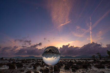 A mesmerizing sunset over a rocky shoreline captured through a glass crystal ball, creating a...