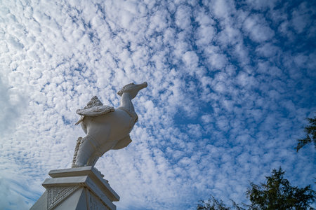 A striking white sculpture stands tall beneath a textured cloudy sky, its graceful form contrasting with the fluffy clouds drifting across the vast blue horizon.の写真素材