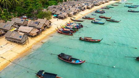 Phang Nga, Thailand-March,20,2025:  A stunning aerial view of a tropical beach with rows of small huts along the coastline, surrounded by lush green jungle. fishing boats are anchoredの写真素材