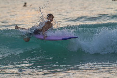 As a soft wave curls behind him, a boy balances skillfully on his surfboard, surrounded by turquoise...