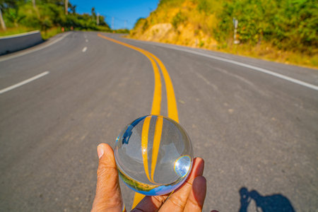 Crystal ball reflection shows an inverted mountain landscape and open road leading into a sea of mist, representing perspective, destiny, and exploration. The curve road strect ahead to the mistの写真素材