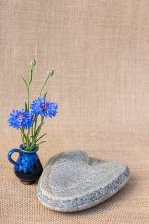 A stone heart and next to it blue cornflowers in a small vase.の写真素材