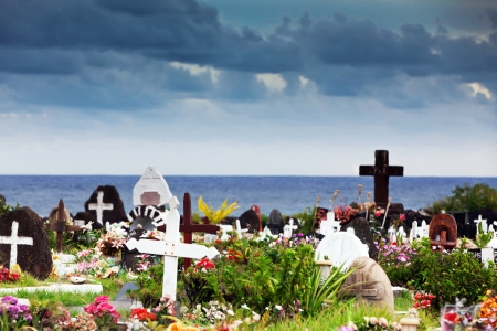 Memorial stones and colourful flowers in a graveyard in Hanga Roa, Easter Island, under thundery skyのeditorial素材